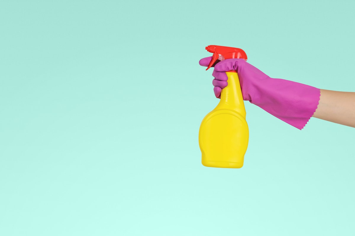 Gloved hand holding yellow spray bottle against mint background